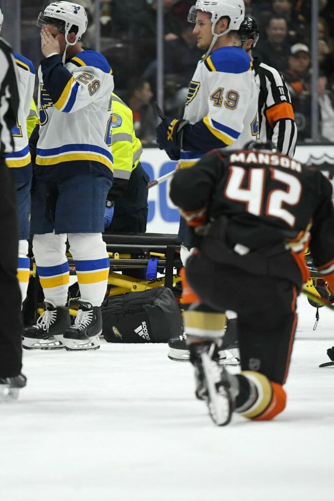 St. Louis Blues defenseman Vince Dunn, left, wipes his face as Anaheim Ducks defenseman Josh Manson kneels on the ice while Blues defenseman Jay Bouwmeester, who suffered a medical emergency, is worked on by medical personnel during the first period of the game, Feb. 11, 2020, in Anaheim, California.